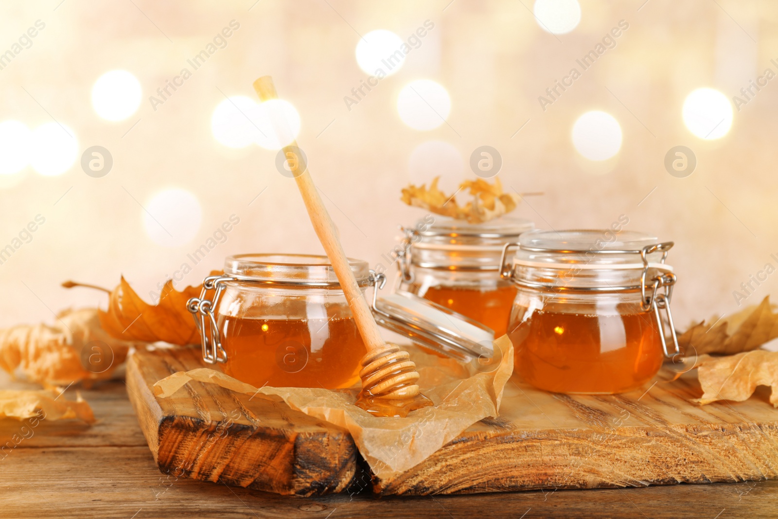 Photo of Dipper and jars with honey on table against blurred lights