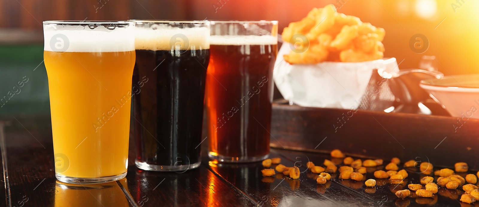 Image of Glasses of tasty beer and snacks on wooden table in bar. Banner design