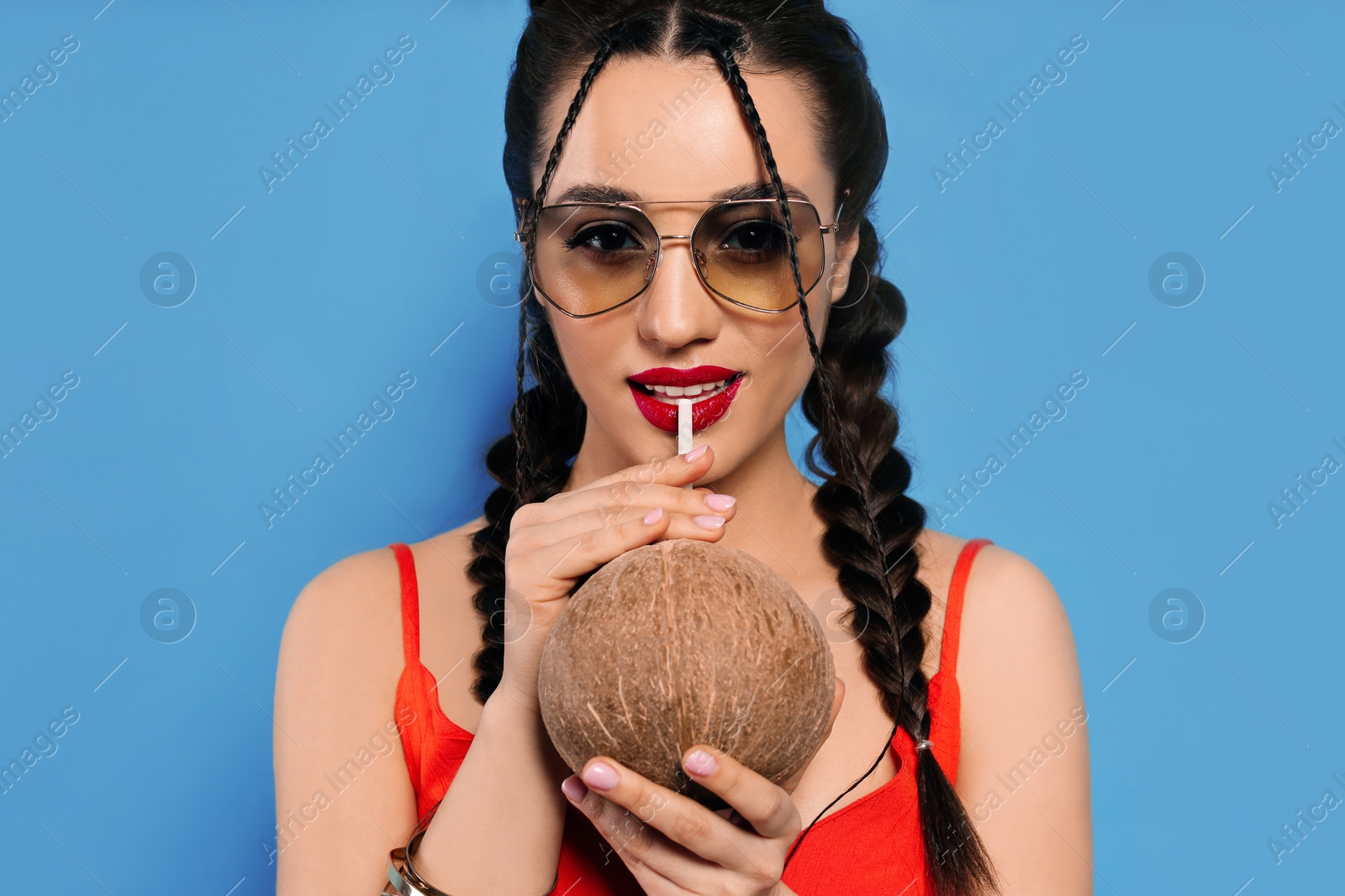 Photo of Young woman with fresh coconut on light blue background. Exotic fruit