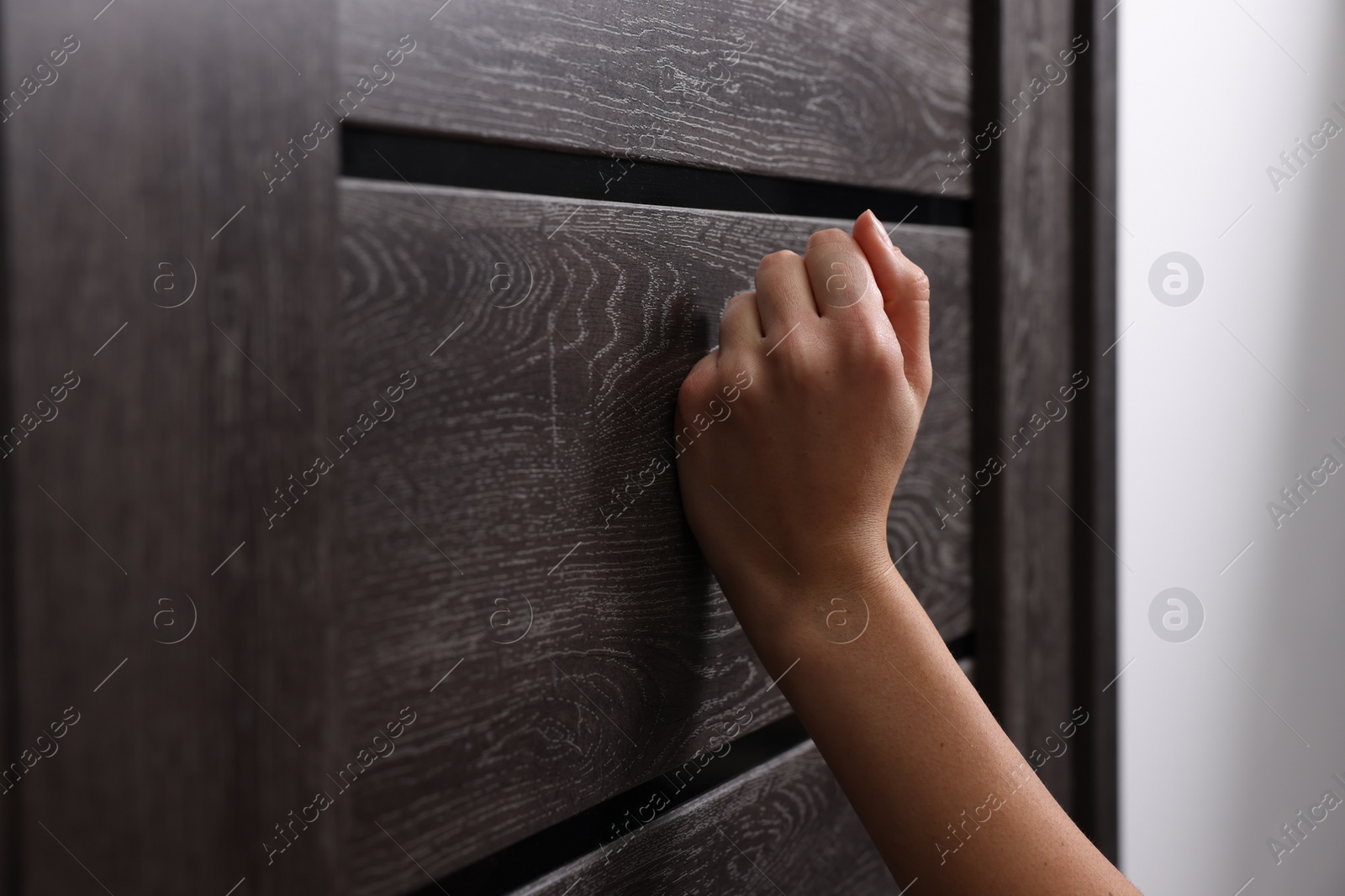 Photo of Woman knocking on door indoors, closeup view