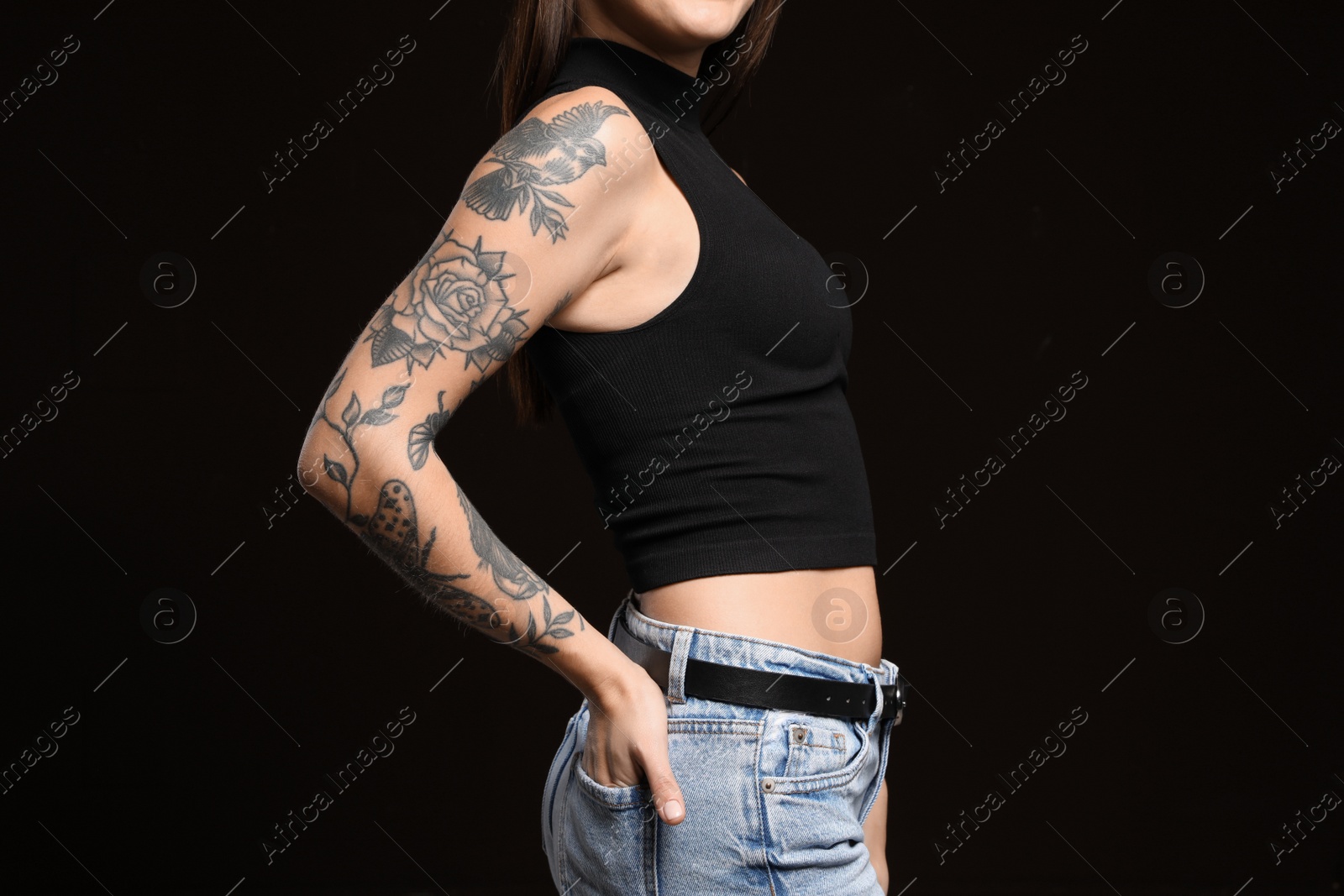 Photo of Beautiful woman with tattoos on arm against black background, closeup