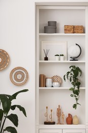 Stylish shelves with decorative elements and houseplants near white wall. Interior design