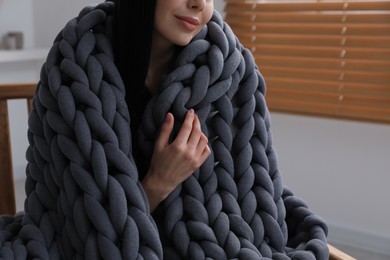 Photo of Woman with chunky knit blanket in armchair at home, closeup