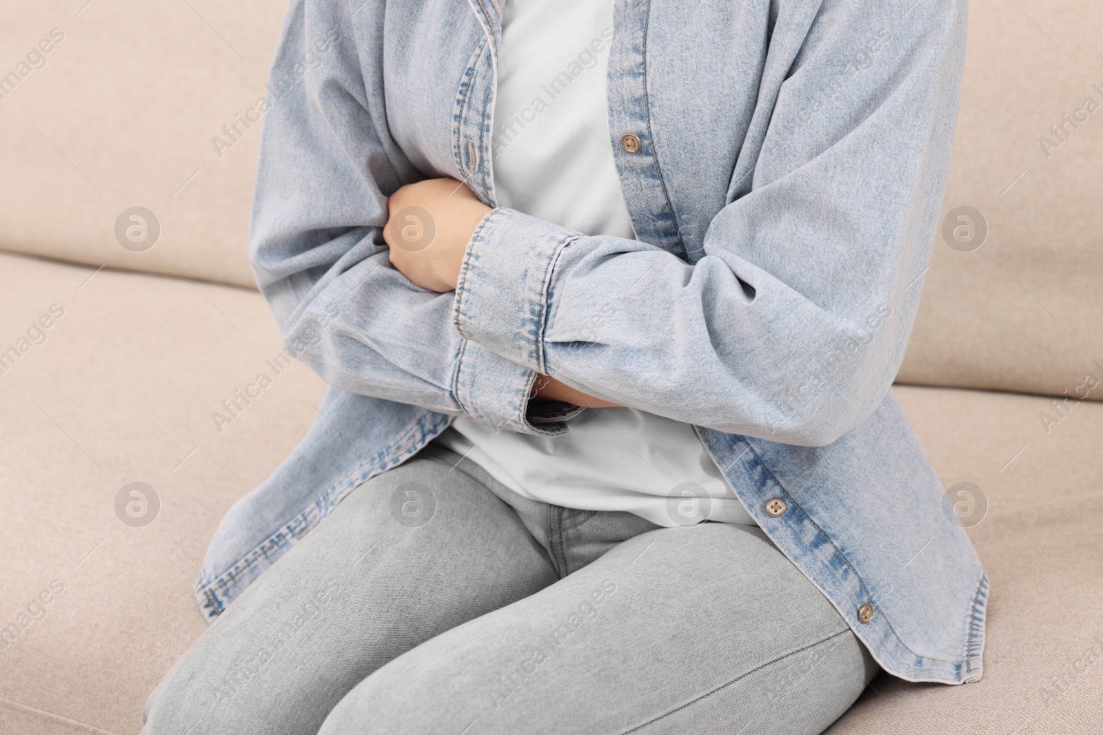 Photo of Young woman suffering from stomach pain on sofa, closeup