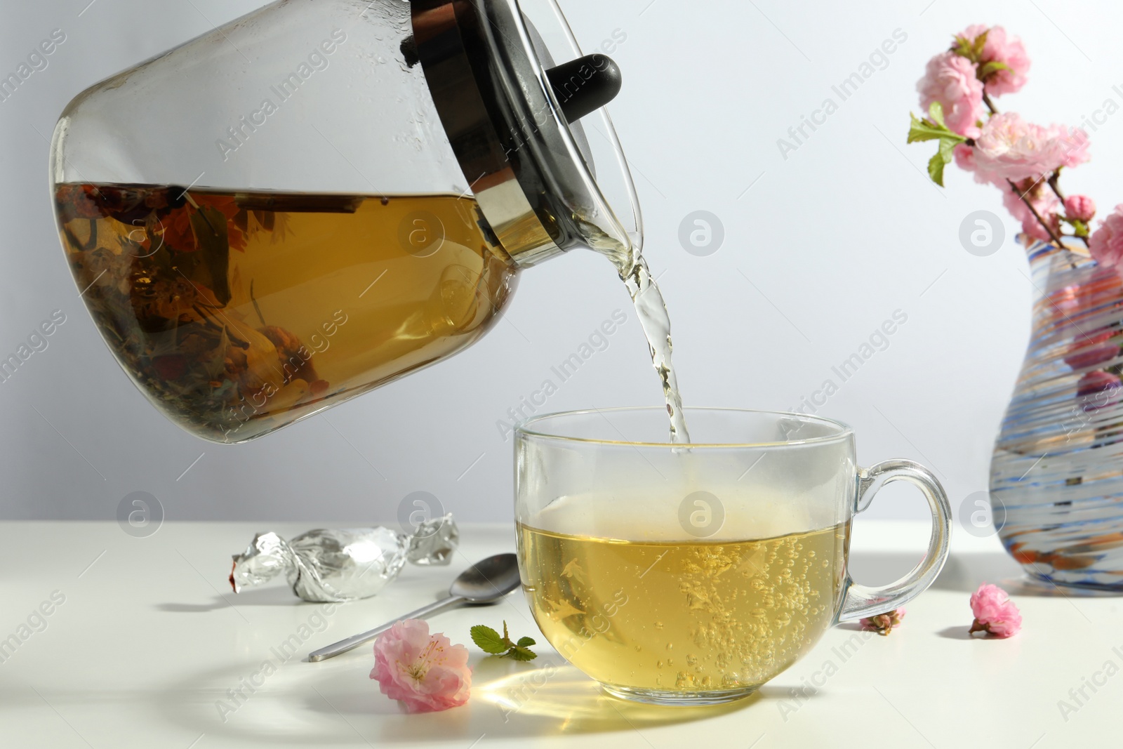 Photo of Pouring freshly brewed tea into glass cup at white table