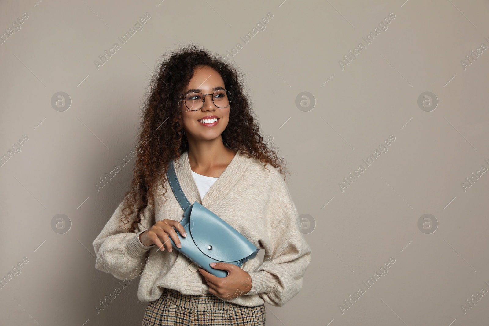 Photo of Beautiful African American woman with stylish waist bag on beige background, space for text