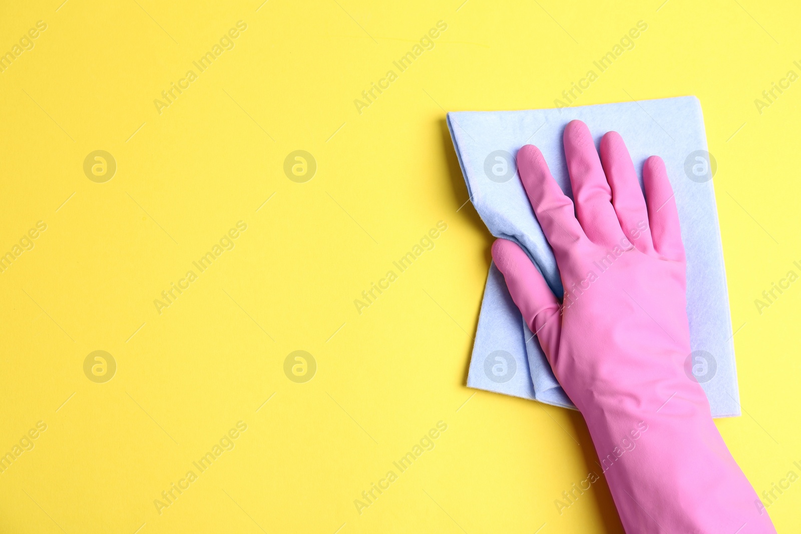 Photo of Person in rubber glove with rag on yellow background, closeup of hand. Space for text