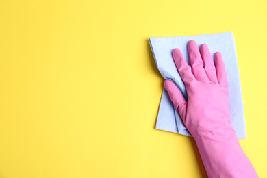 Photo of Person in rubber glove with rag on yellow background, closeup of hand. Space for text