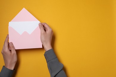 Photo of Woman holding letter envelope with card at orange table, top view. Space for text