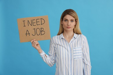 Unemployed woman holding sign with phrase I Need A job on light blue background
