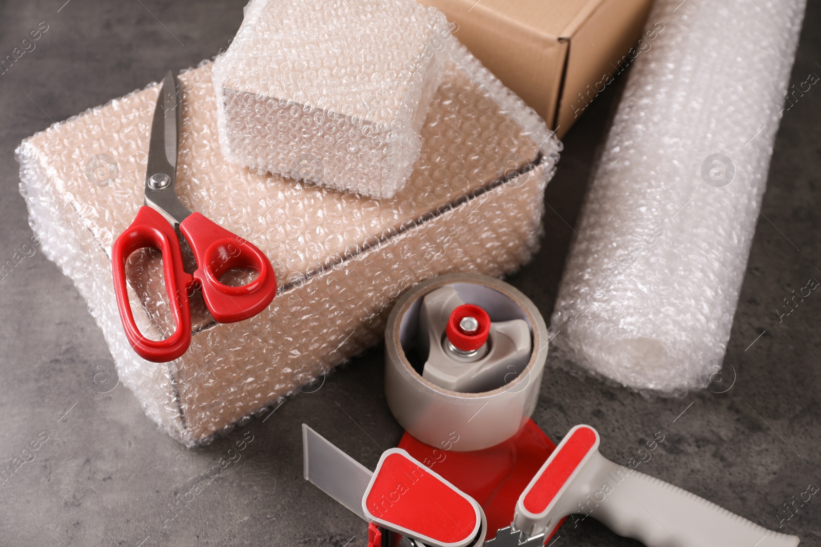 Photo of Cardboard boxes, bubble wrap, adhesive tape and scissors on dark grey table