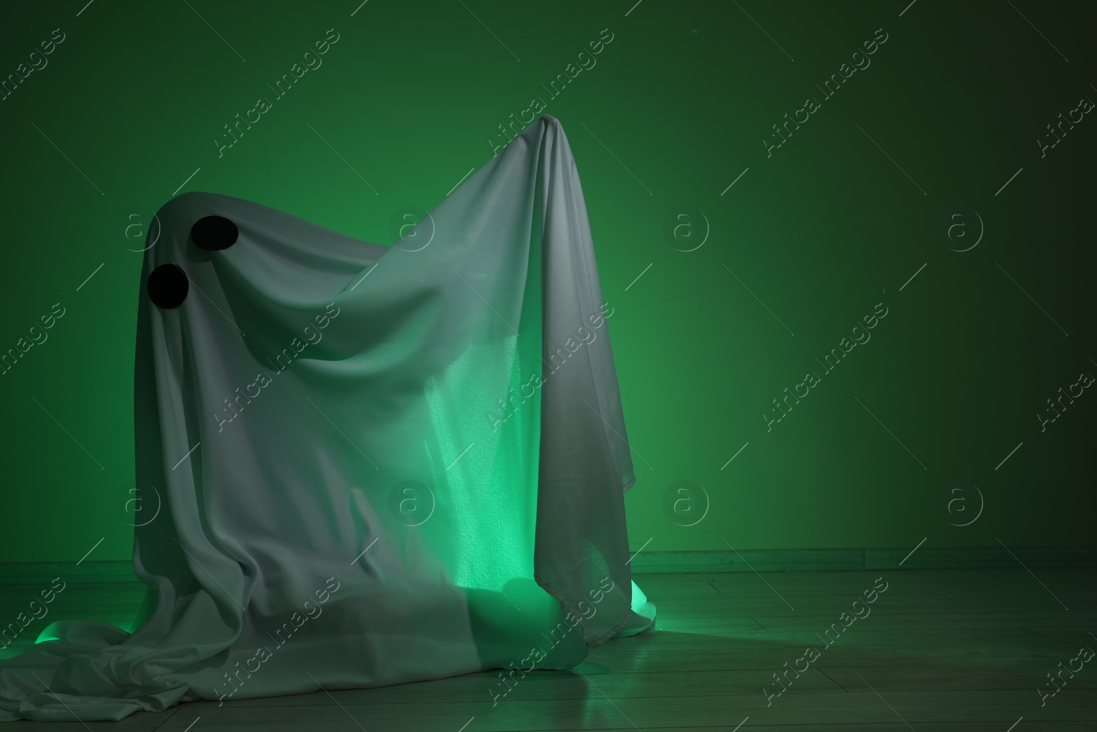 Photo of Creepy ghost. Woman covered with sheet in green light, space for text