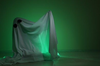 Creepy ghost. Woman covered with sheet in green light, space for text