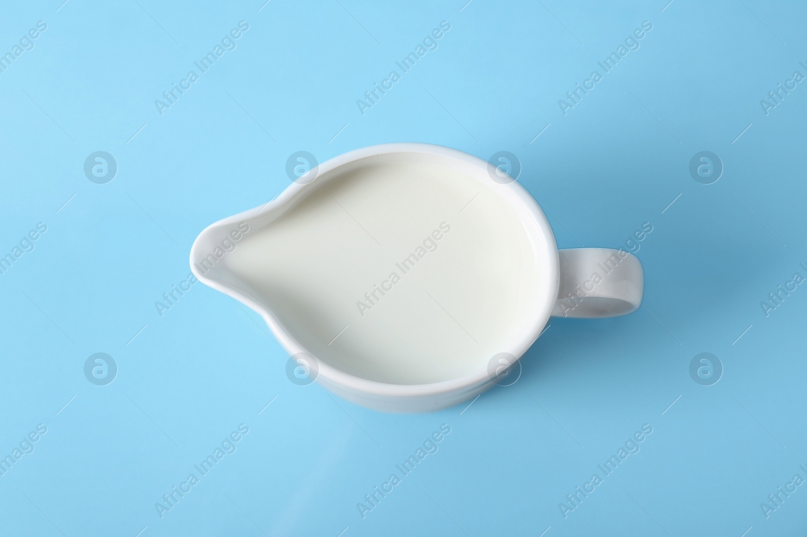 Photo of Jug of fresh milk on light blue background, top view