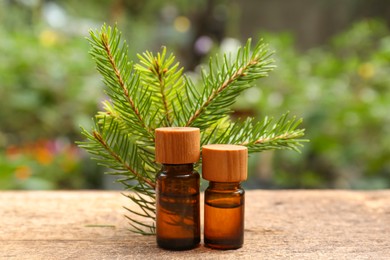 Photo of Bottles of pine essential oil and conifer tree branches on wooden table, closeup