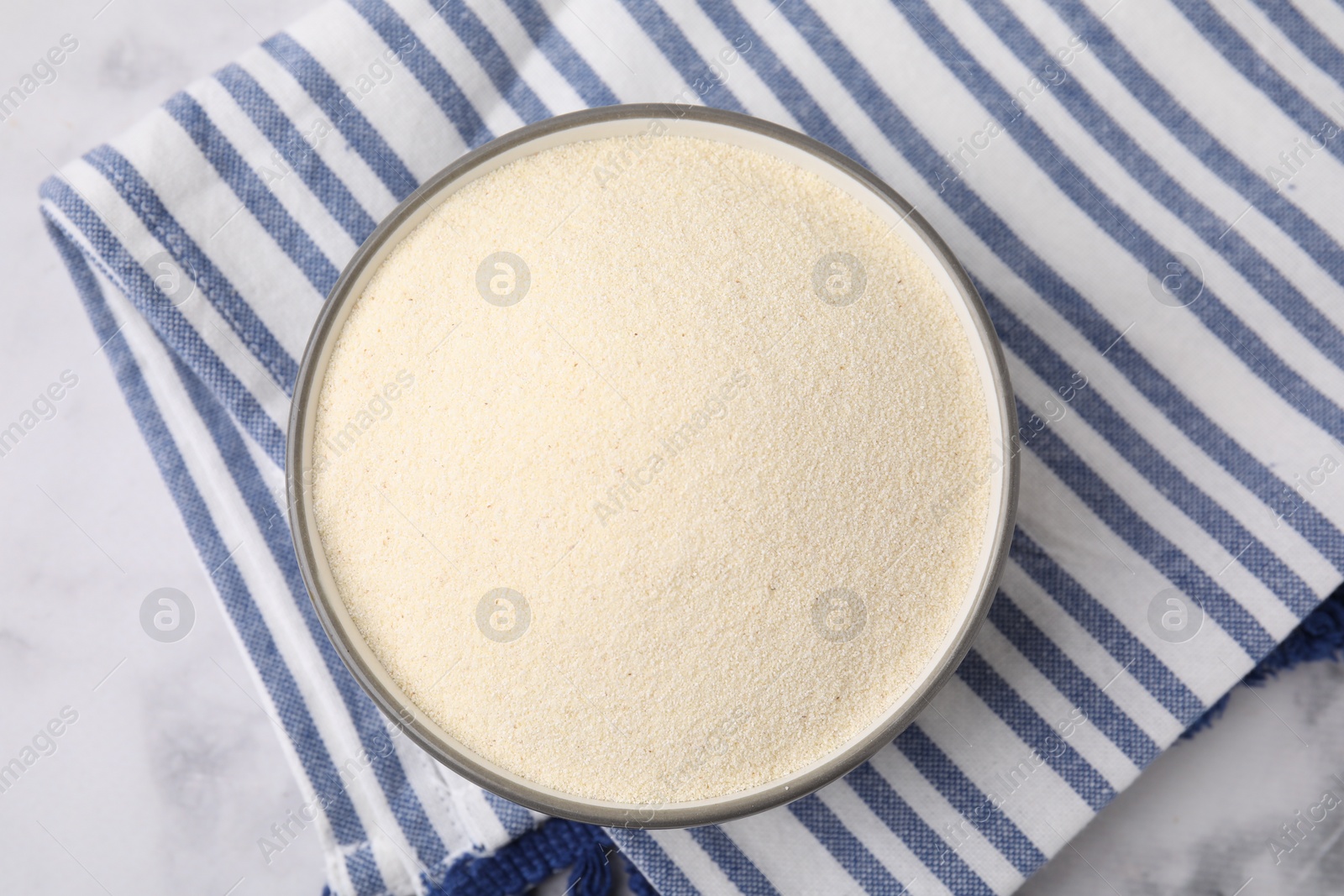 Photo of Bowl of uncooked organic semolina on white marble table, top view