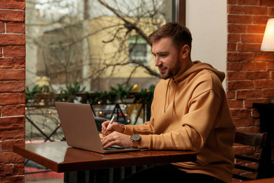 Male blogger working with laptop at table in cafe
