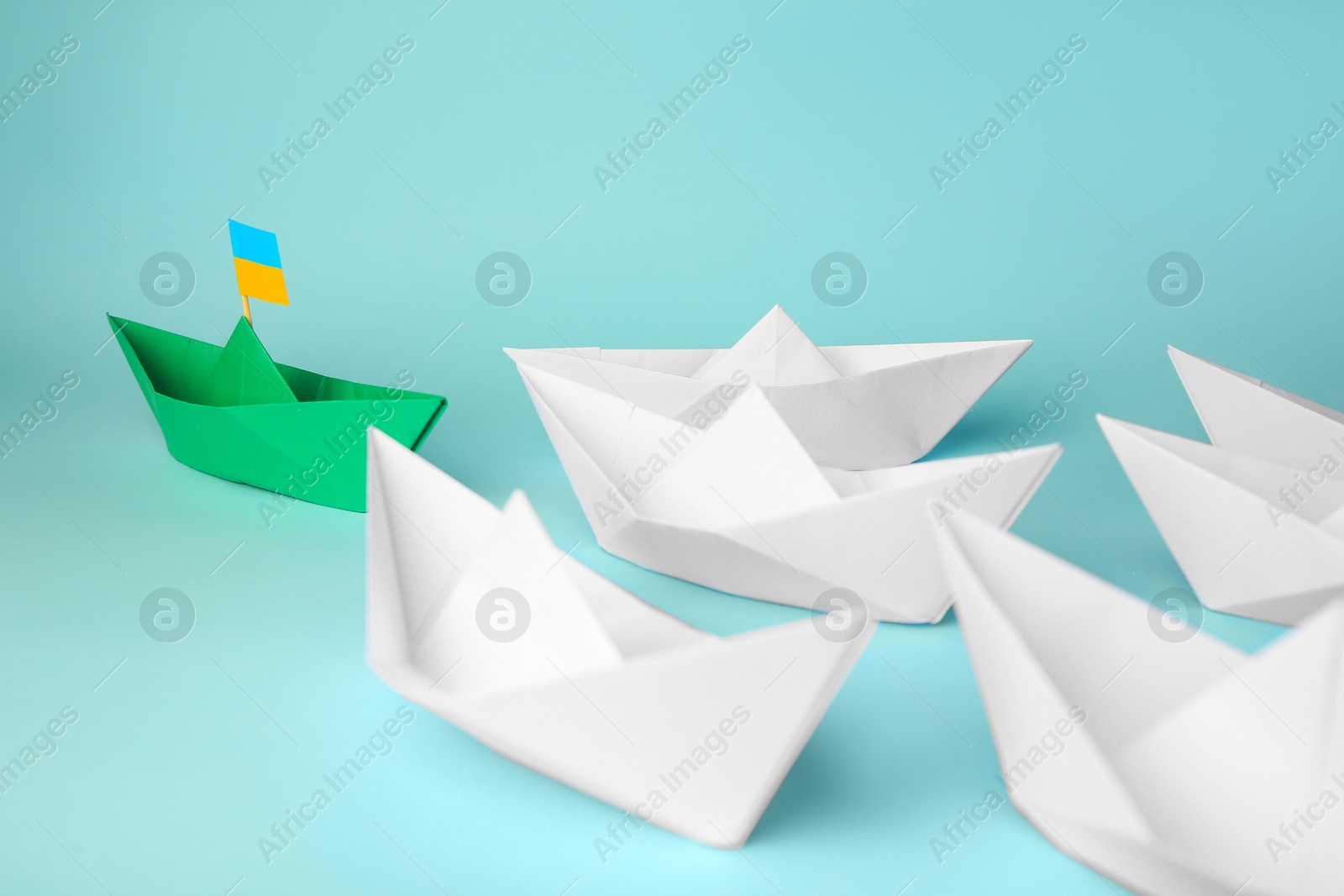 Photo of Group of paper boats following green one on light blue background. Leadership concept