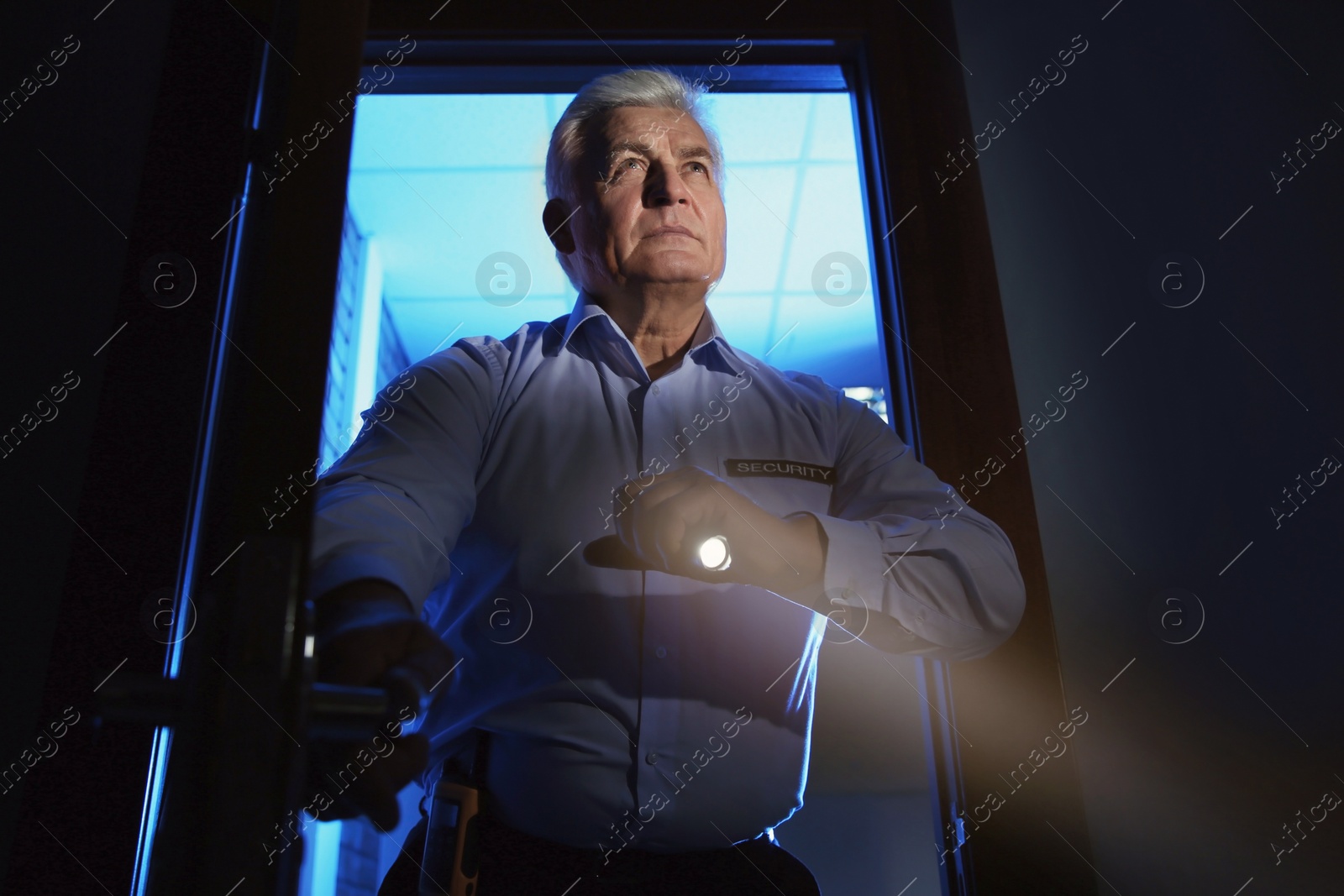 Photo of Professional security guard with flashlight checking dark room