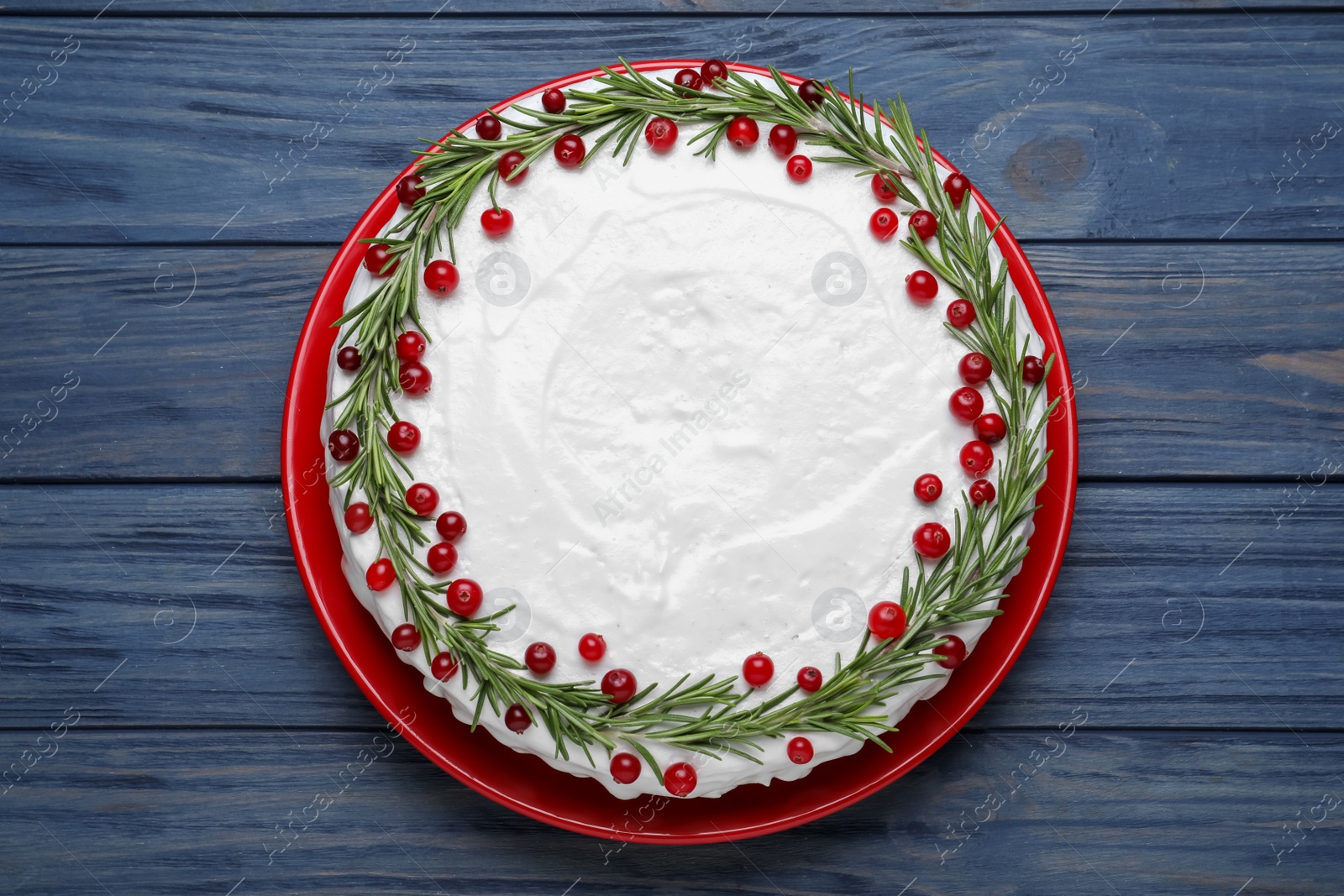 Photo of Traditional Christmas cake decorated with rosemary and cranberries on blue wooden table, top view