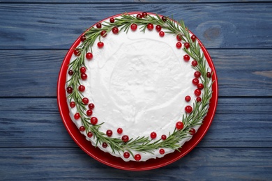 Photo of Traditional Christmas cake decorated with rosemary and cranberries on blue wooden table, top view