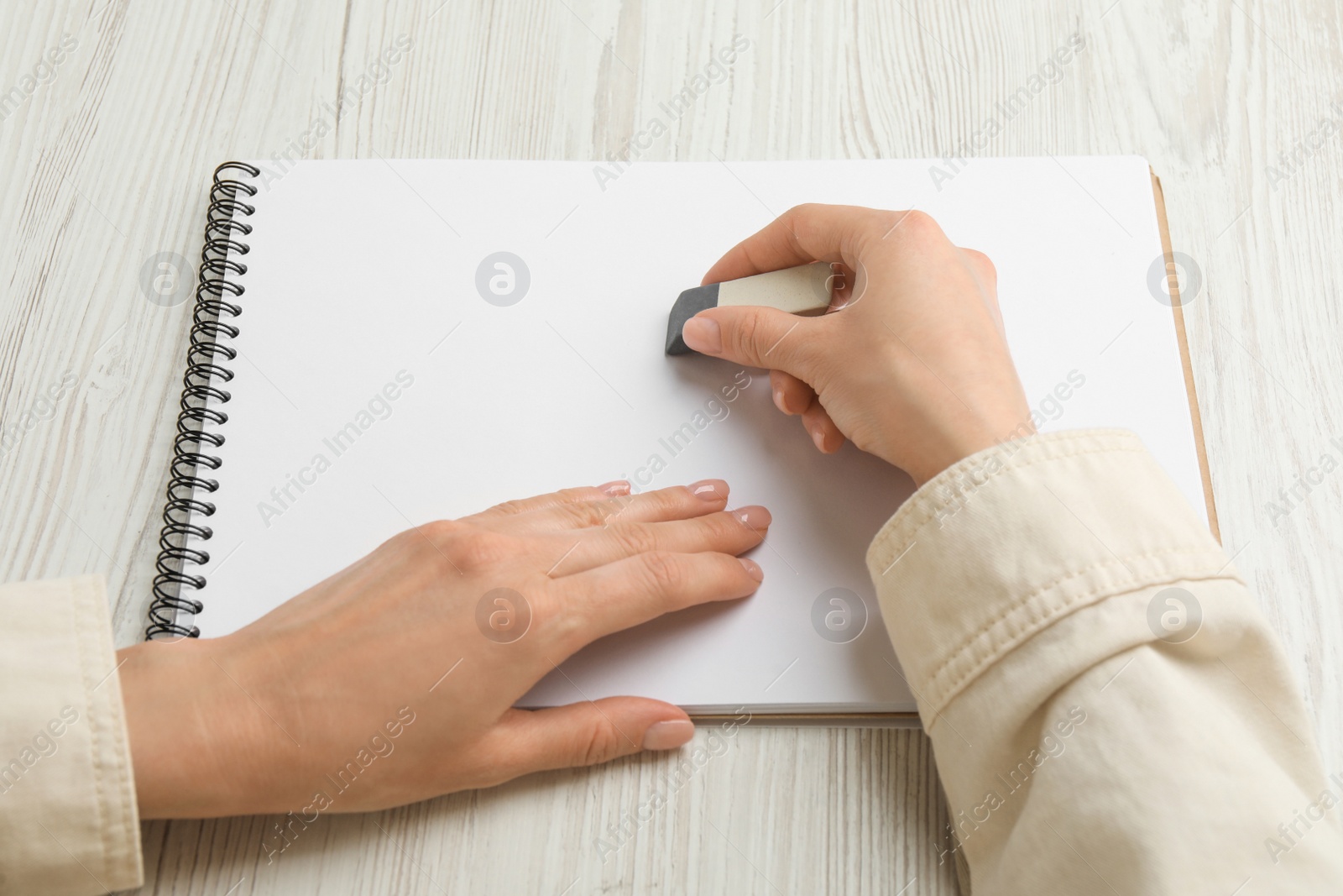 Photo of Woman erasing something in notebook at white wooden table, closeup