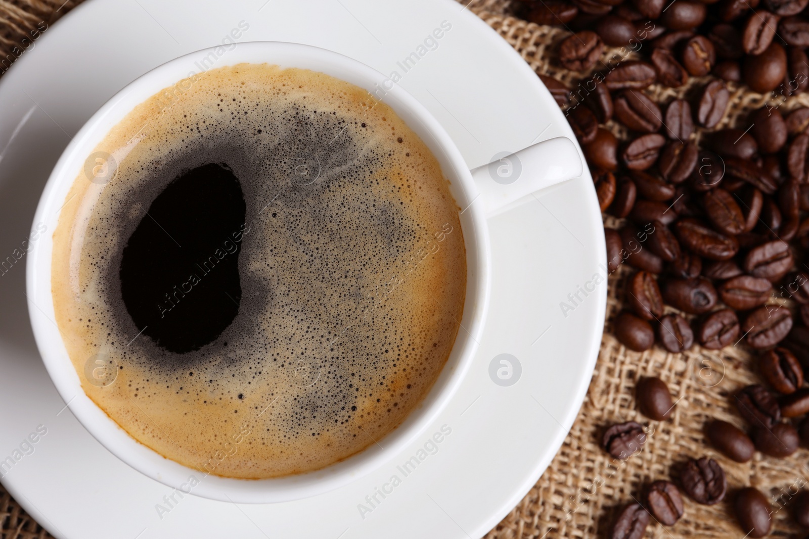 Photo of Cup of hot aromatic coffee and roasted beans on sackcloth, flat lay. Space for text