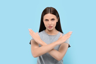 Photo of Stop gesture. Woman with crossed hands on light blue background