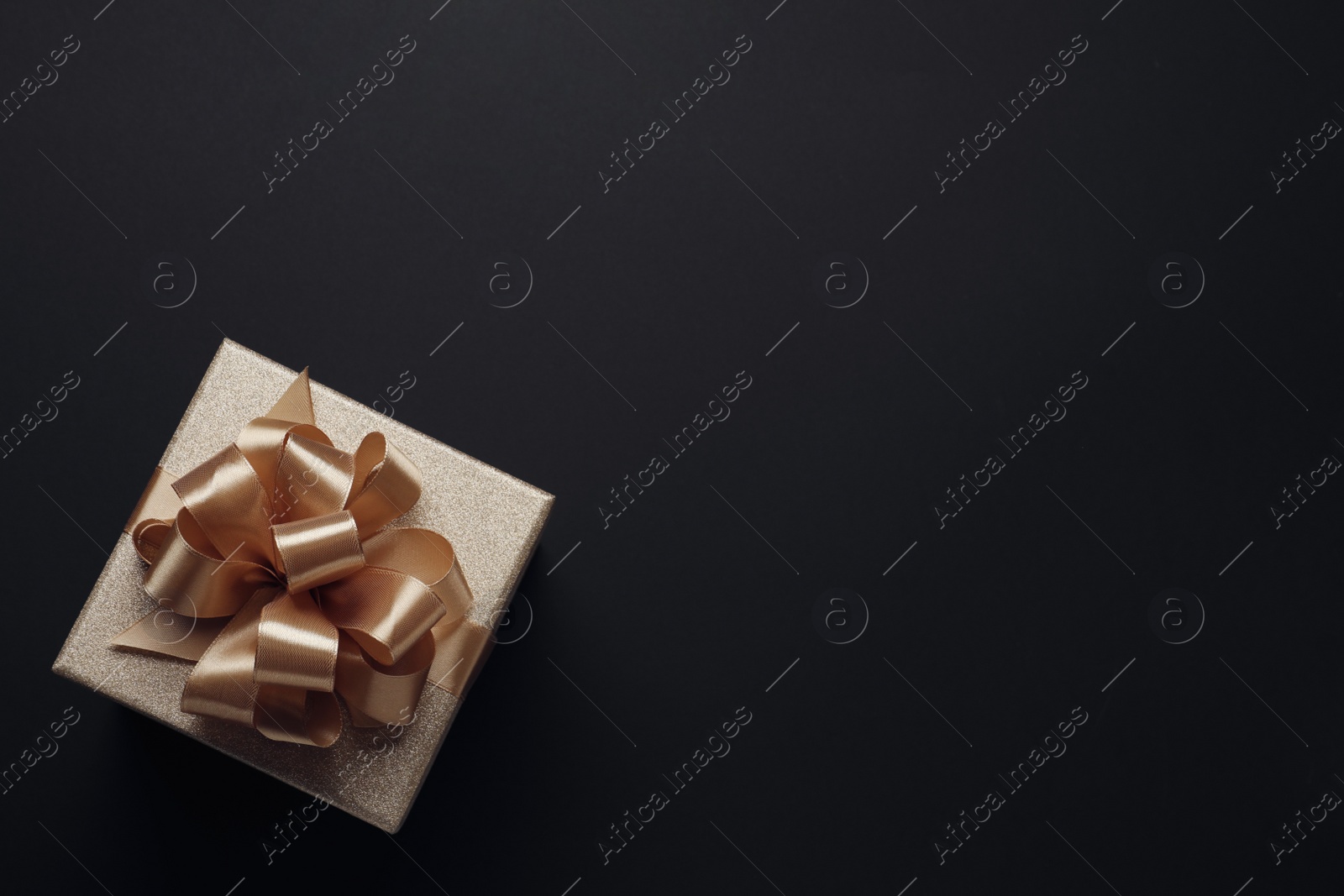 Photo of Golden gift box with satin bow on black background. top view. Space for text