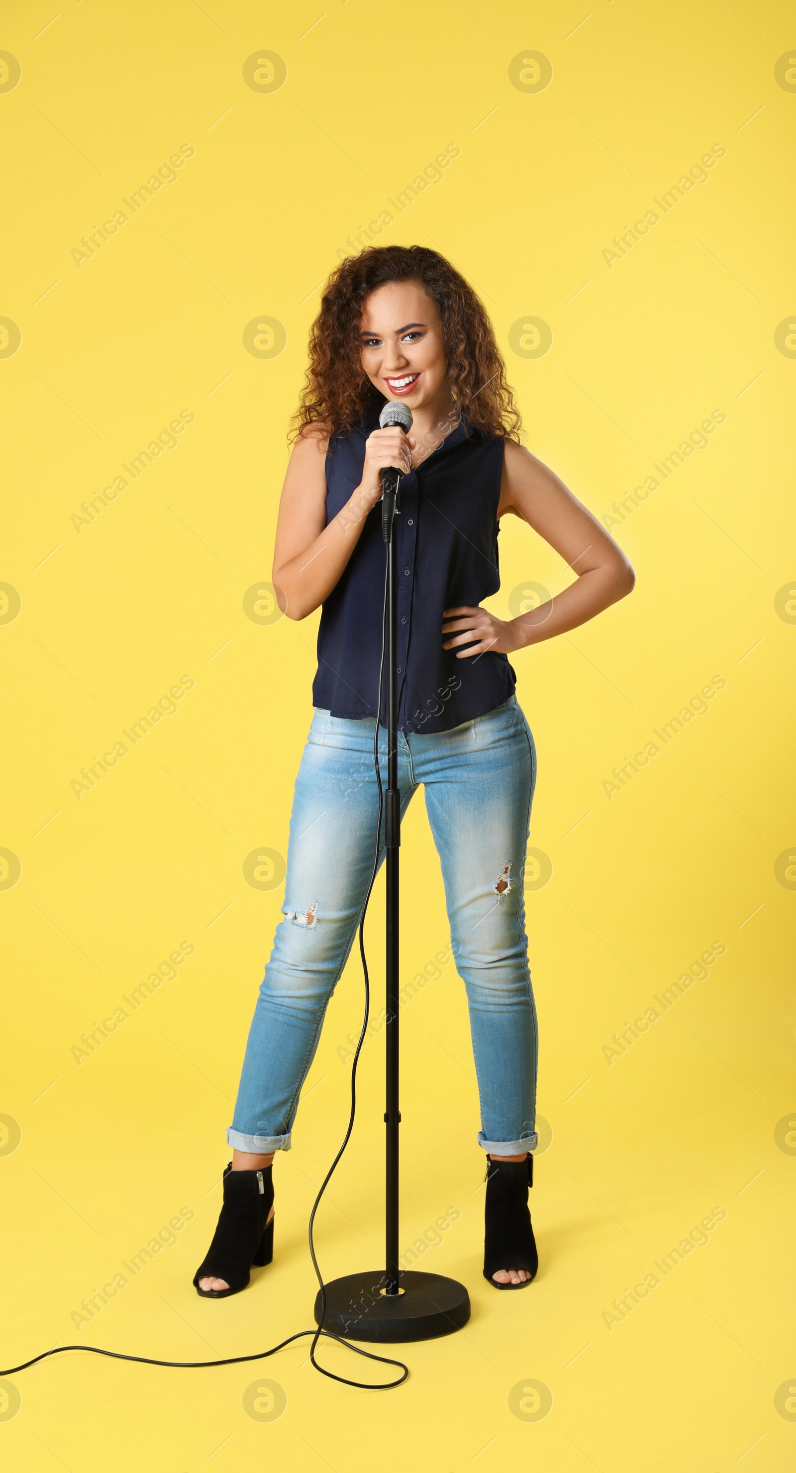 Photo of Curly African-American woman posing with microphone on color background