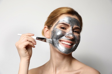 Beautiful woman applying mask onto face against light background