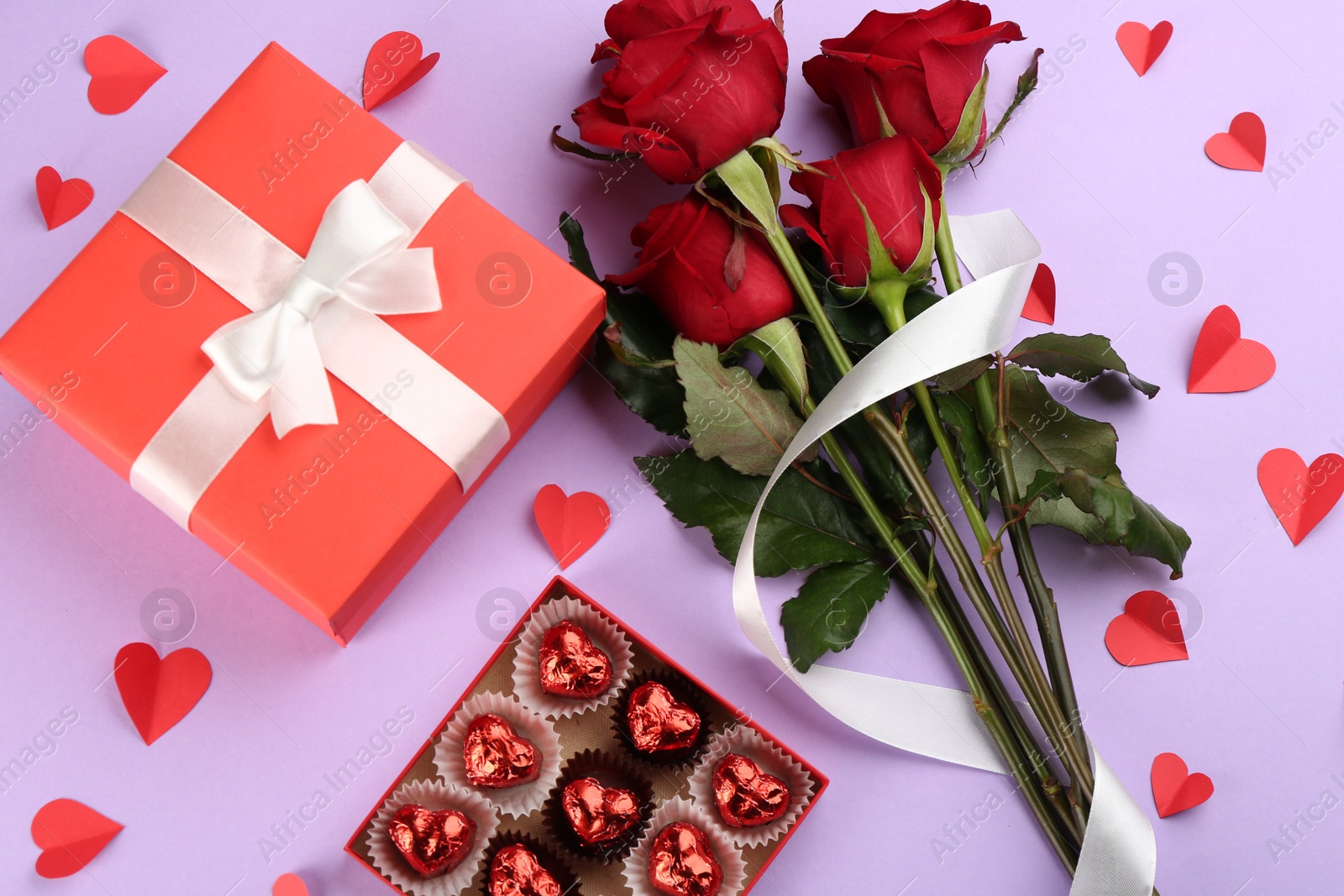 Photo of Flat lay composition with beautiful red roses and gift box on violet background. Valentine's Day celebration