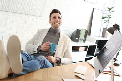 Photo of Young man with cup of drink relaxing at table in office during break