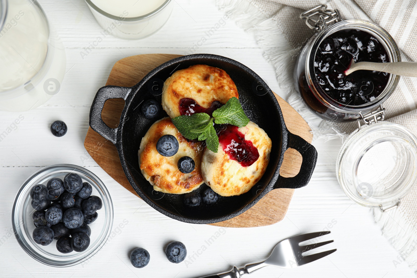 Photo of Delicious cottage cheese pancakes with blueberries, mint and jam on white wooden table, flat lay