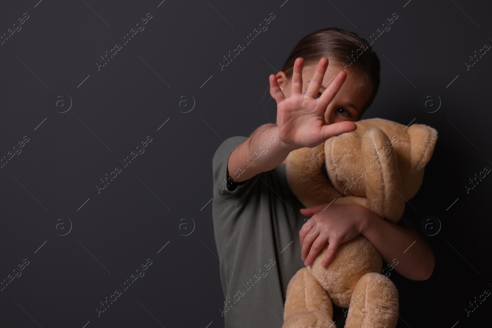 Photo of Child abuse. Girl with toy making stop gesture near grey wall, selective focus. Space for text