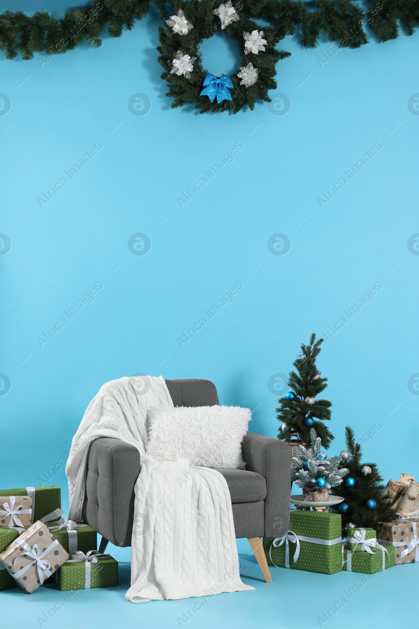 Photo of Beautiful Christmas themed photo zone with stylish armchair, trees and gift boxes on light blue background