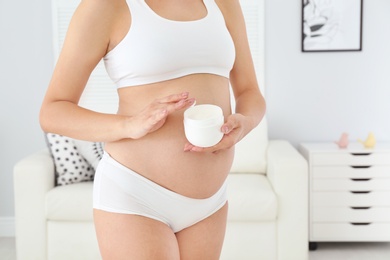 Pregnant woman holding body cream at home, closeup