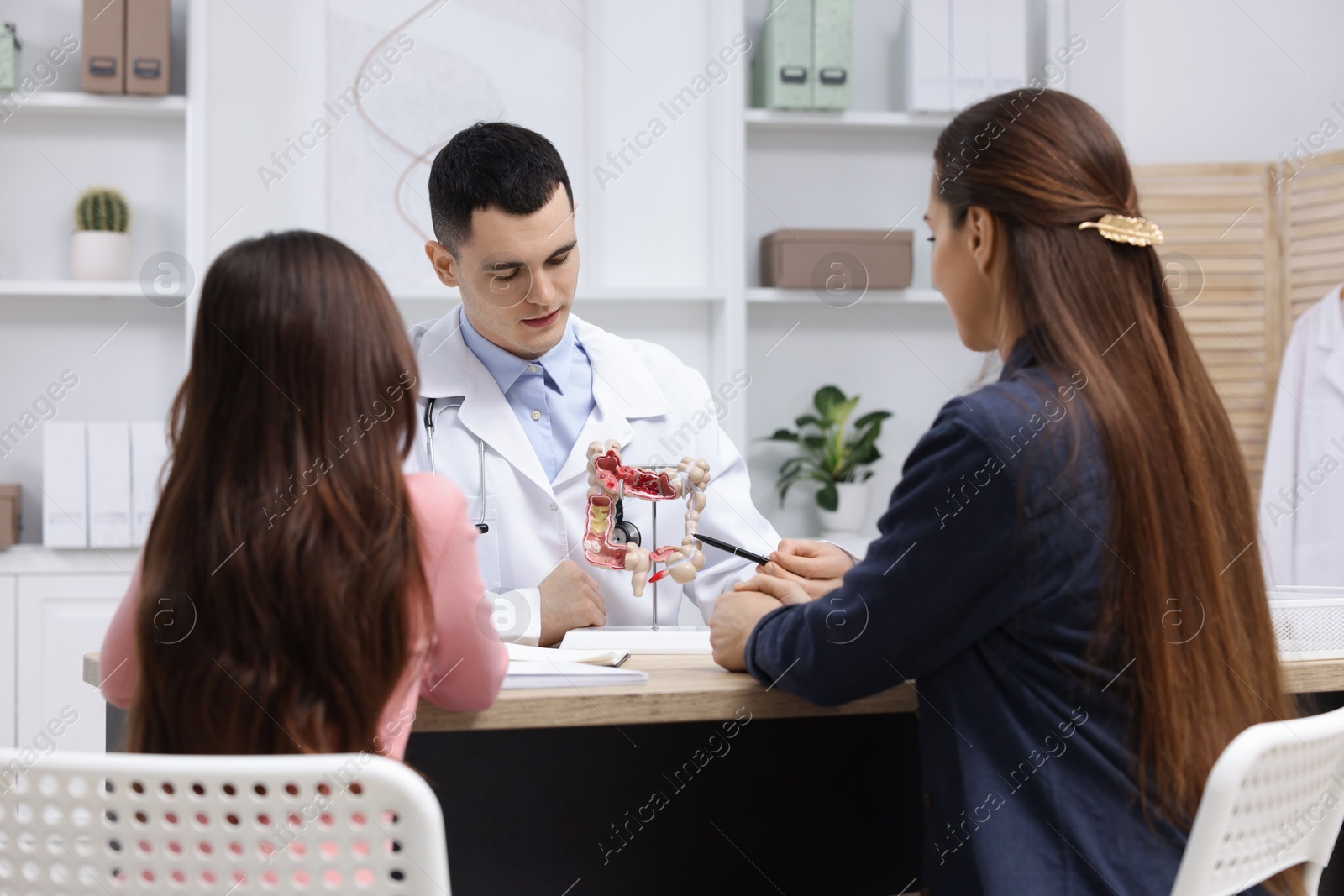 Photo of Gastroenterologist with model of intestine consulting woman and her daughter in clinic