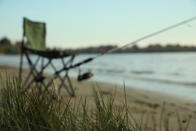Blurred view of folding chair and fishing rod at riverside