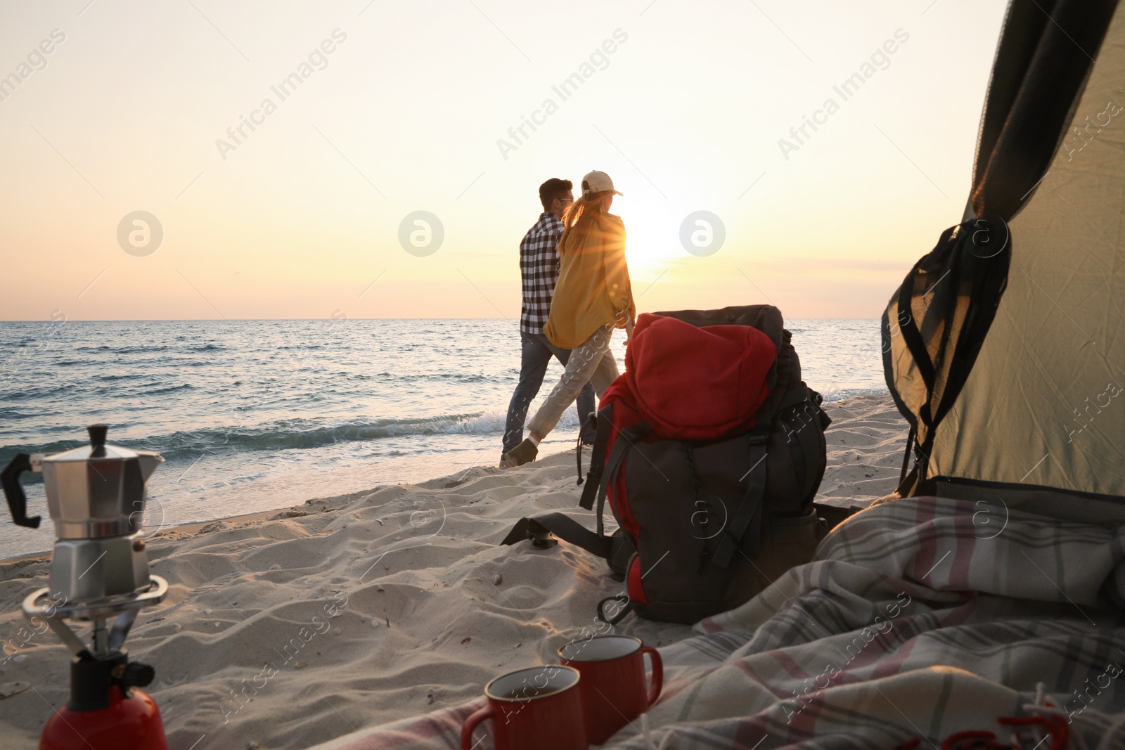 Photo of Couple walking by sea at sunset, view from camping tent