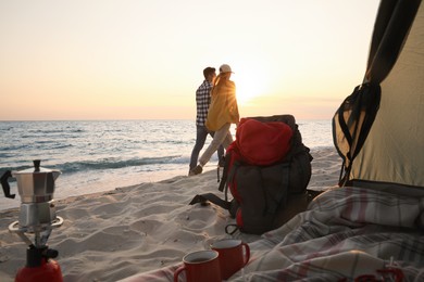 Couple walking by sea at sunset, view from camping tent