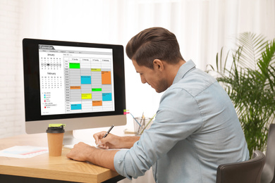 Photo of Handsome man planning his schedule with calendar app on computer in office