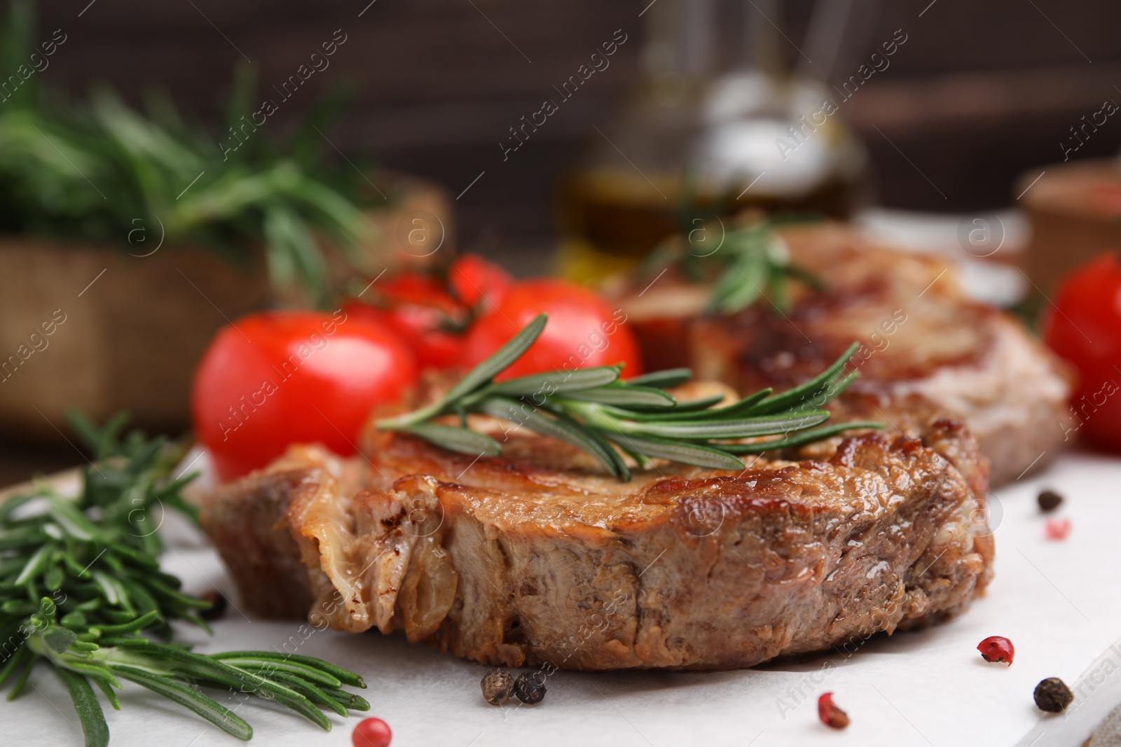 Photo of Delicious fried meat with rosemary, tomatoes and spices on white table, closeup