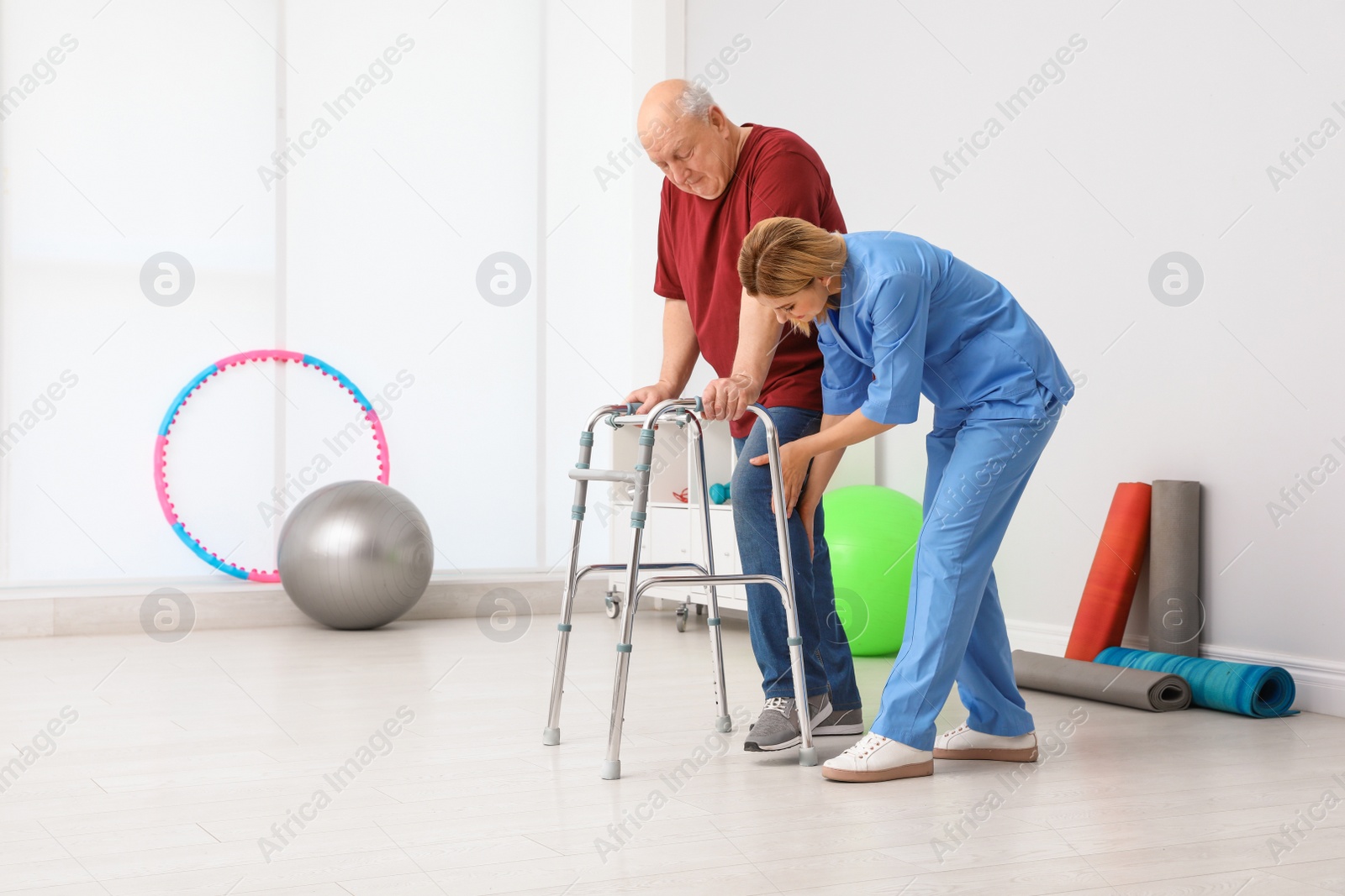 Photo of Caretaker helping elderly man with walking frame indoors