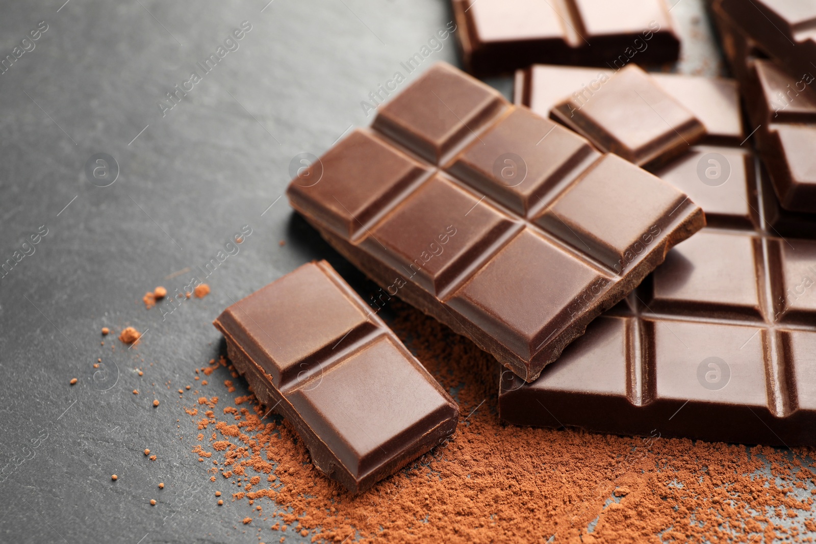 Photo of Delicious dark chocolate and cocoa powder on black table, closeup