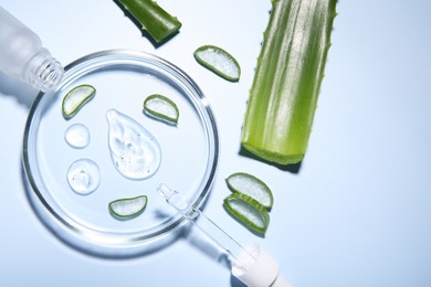 Photo of Cut aloe vera, bottle and drops of cosmetic gel on light blue background, flat lay. Space for text