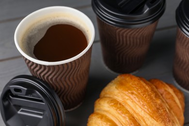 Photo of Coffee to go. Paper cups with tasty drink and croissant on grey table, closeup