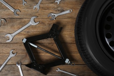Photo of Car wheel, scissor jack and wrench set on wooden surface, flat lay