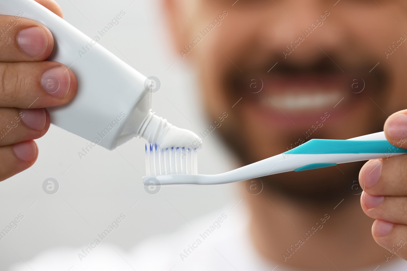 Photo of Man applying toothpaste on brush against blurred background, closeup