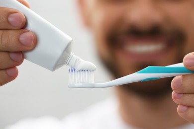 Photo of Man applying toothpaste on brush against blurred background, closeup